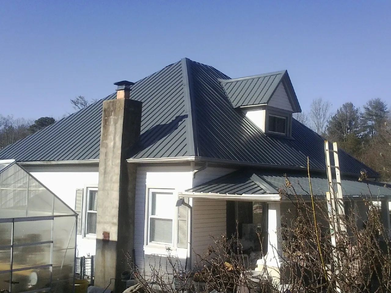 Dark blue standing seam metal roof on a white farmhouse with dormer — Slate & Tile Roof Repair by Roofing Brothers in Stovall