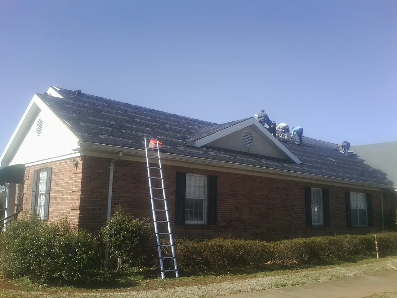 Crew tearing shingles off a brick ranch roof with a ladder set — Emergency Roof Repair work by our crew in Stovall