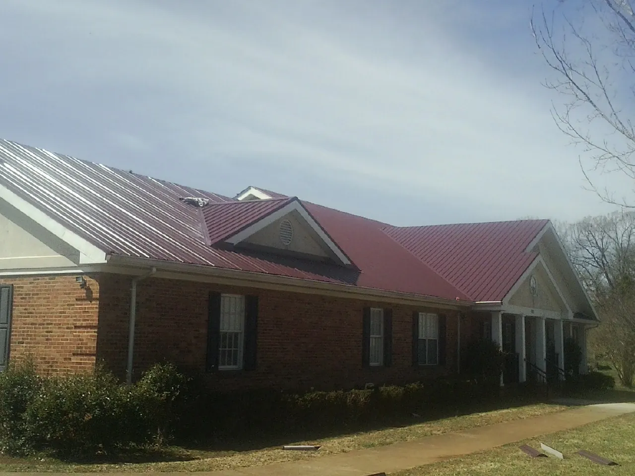 Red metal roof with gabled entries on a long brick building, from a Hail Damage Roof Repair job in Stovall