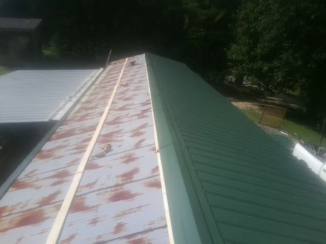Old rusted panels beside newly installed green metal roofing — Wind Damage Roof Repair by Roofing Brothers in Stovall