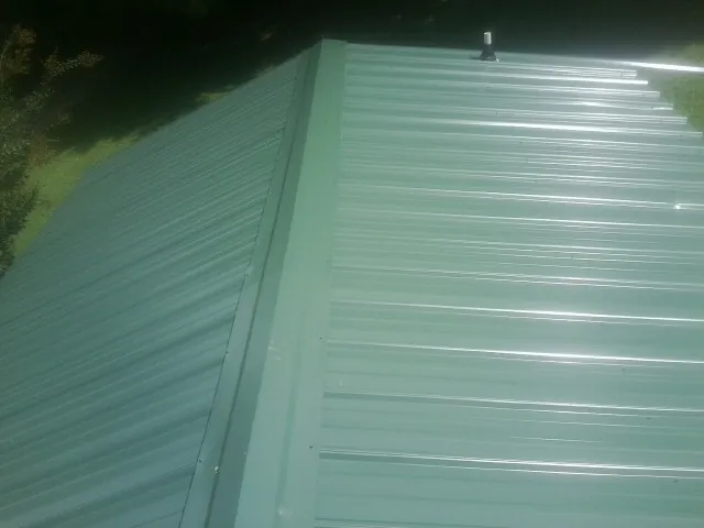 New green metal panels meeting at the ridge of a roof — Flat Roof Repair work by our crew in Stovall