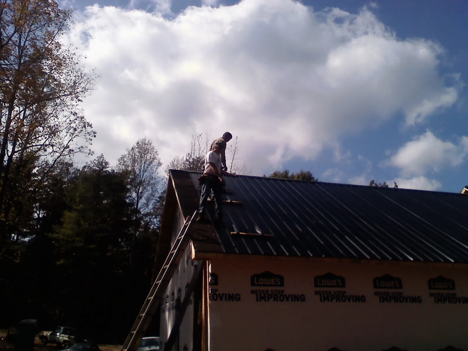 Roofer fastening dark metal panels high against a cloudy sky, from a Roof Inspection job in Stovall