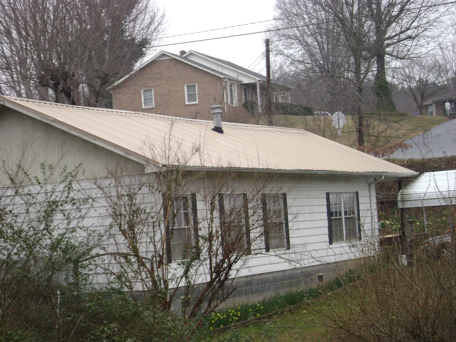 Tan metal roof on a white sided house set into a hillside — Commercial Roofing by Roofing Brothers in Stovall